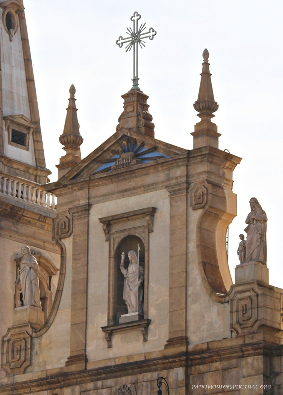 Frontão da igreja, contendo a cruz, o símbolo do Cordeiro (Apocalipse cap. 5) sobre o livro de sete selos (dentro do triângulo azul), e as três virtudes teologais: a Esperança (esquerda), a Fé (centro), e a Caridade (direita)