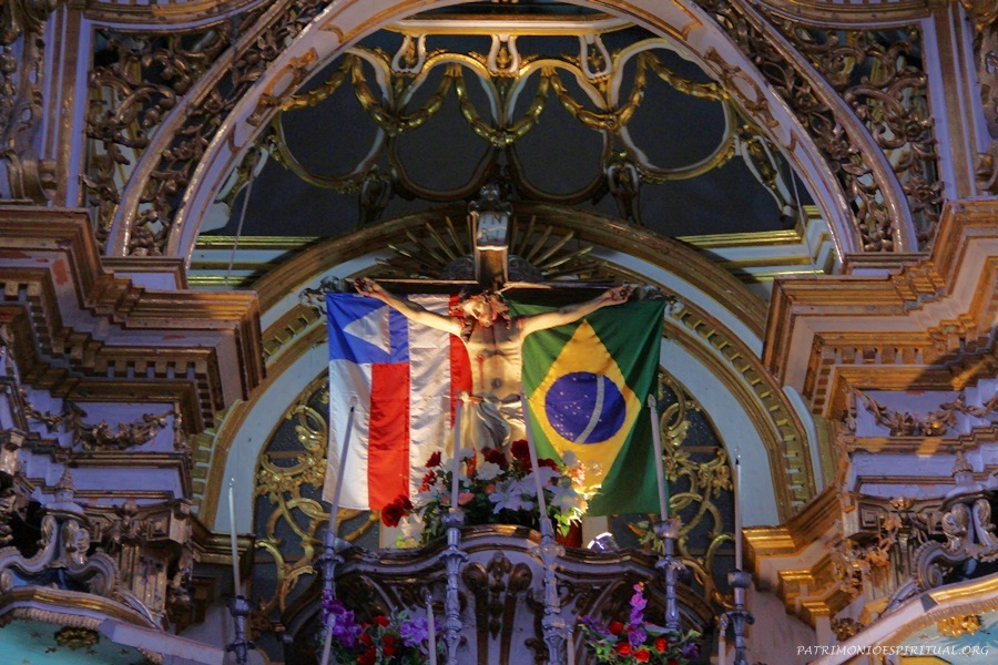 Crucifixo do altar mor, entre as bandeiras da Bahia e do Brasil.